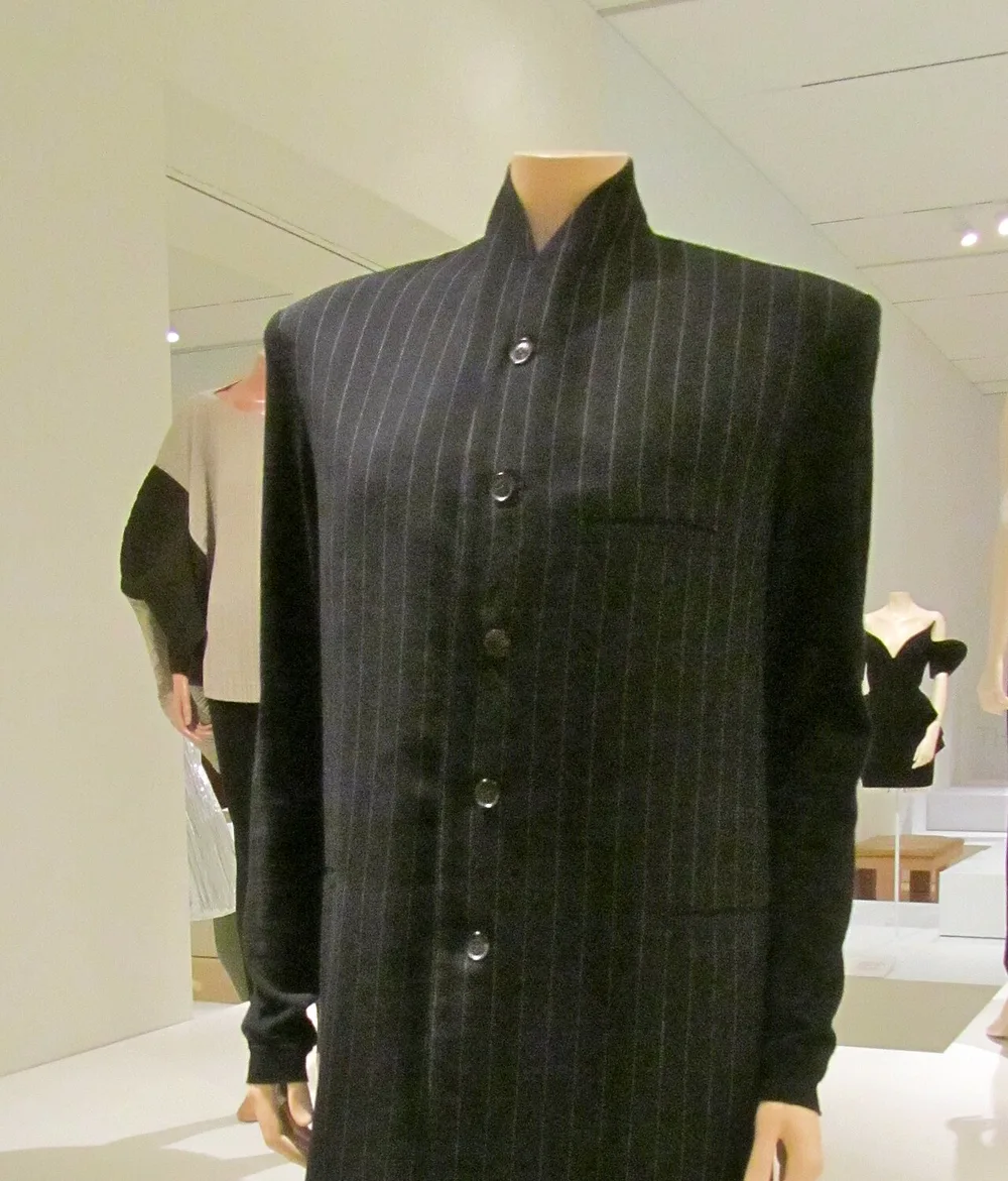 A Yohji Yamamoto black pinstripe wool coat on a mannequin in a museum display